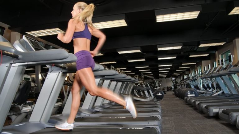 Mulher com trajes fitness correndo na esteira antes ou depois do treino de musculação